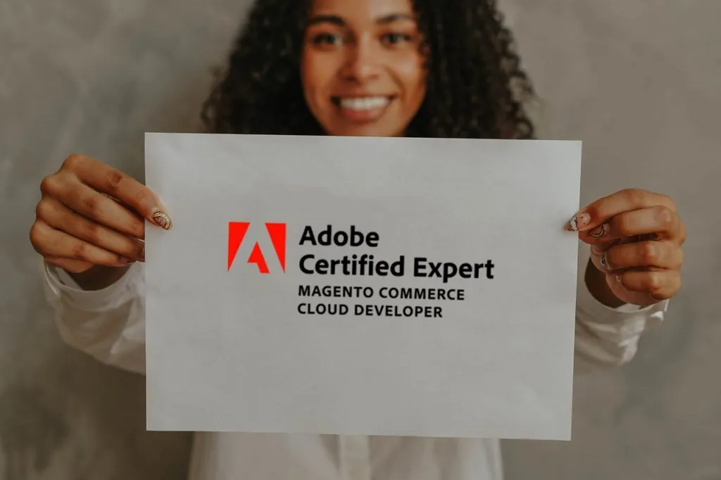 An excited woman holding a Magento Adobe certification